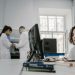 Focused woman working on a computer in a busy laboratory setting, showcasing teamwork and scientific research.