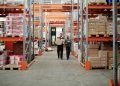 Two workers handle a package in a spacious warehouse surrounded by shelves stocked with boxes and products.