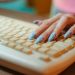 Closeup of a hand with polka dot nails typing on a vintage keyboard, emphasizing retro technology.