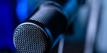 Detailed close-up of a professional studio microphone with a blurred blue background.