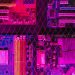 Colorful circuit boards behind a wire mesh, enhanced with pink and purple hues.