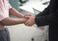 Close-up of a formal handshake between two businessmen in an office environment.