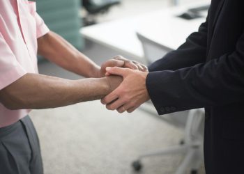 Close-up of a formal handshake between two businessmen in an office environment.