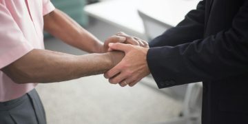 Close-up of a formal handshake between two businessmen in an office environment.