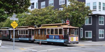Classic San Francisco cable car on Powell and Mason, city streets, greenery, and iconic signs.