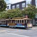 Classic San Francisco cable car on Powell and Mason, city streets, greenery, and iconic signs.