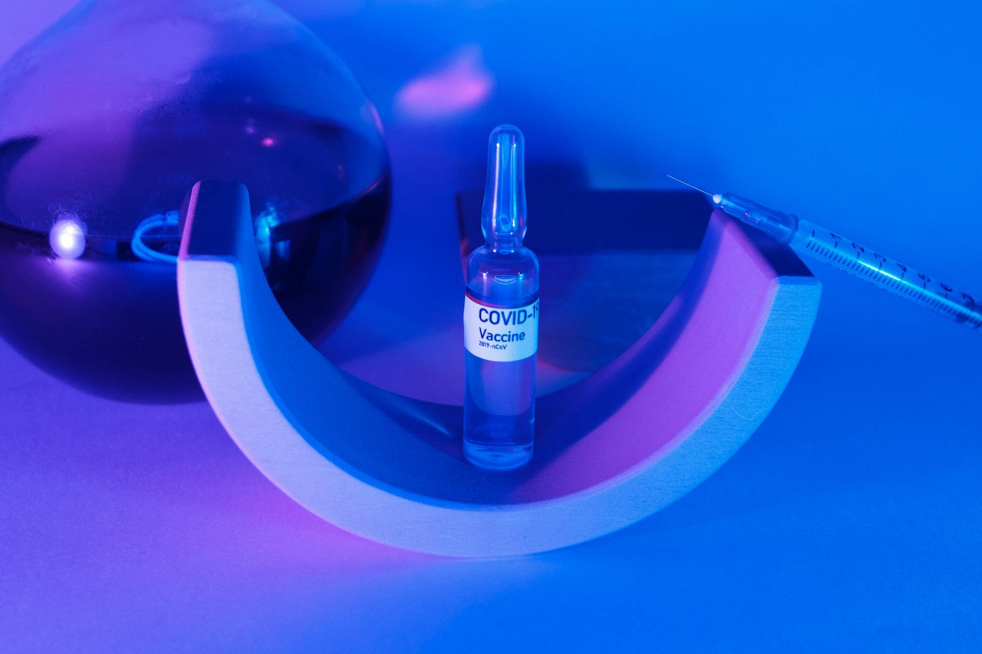 Vaccine for coronavirus for injection with syringe on geometrical decor near glass flask with liquid