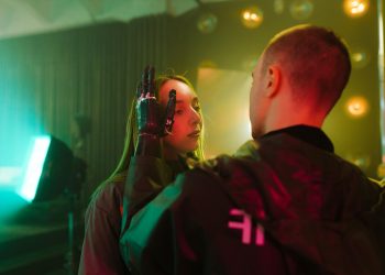 A man with a prosthetic hand gently touches a woman's face in a cyberpunk setting.