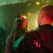 A man with a prosthetic hand gently touches a woman's face in a cyberpunk setting.