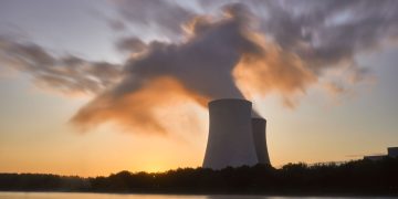 Dramatic image of a nuclear power plant at sunrise with steam rising into a colorful sky.