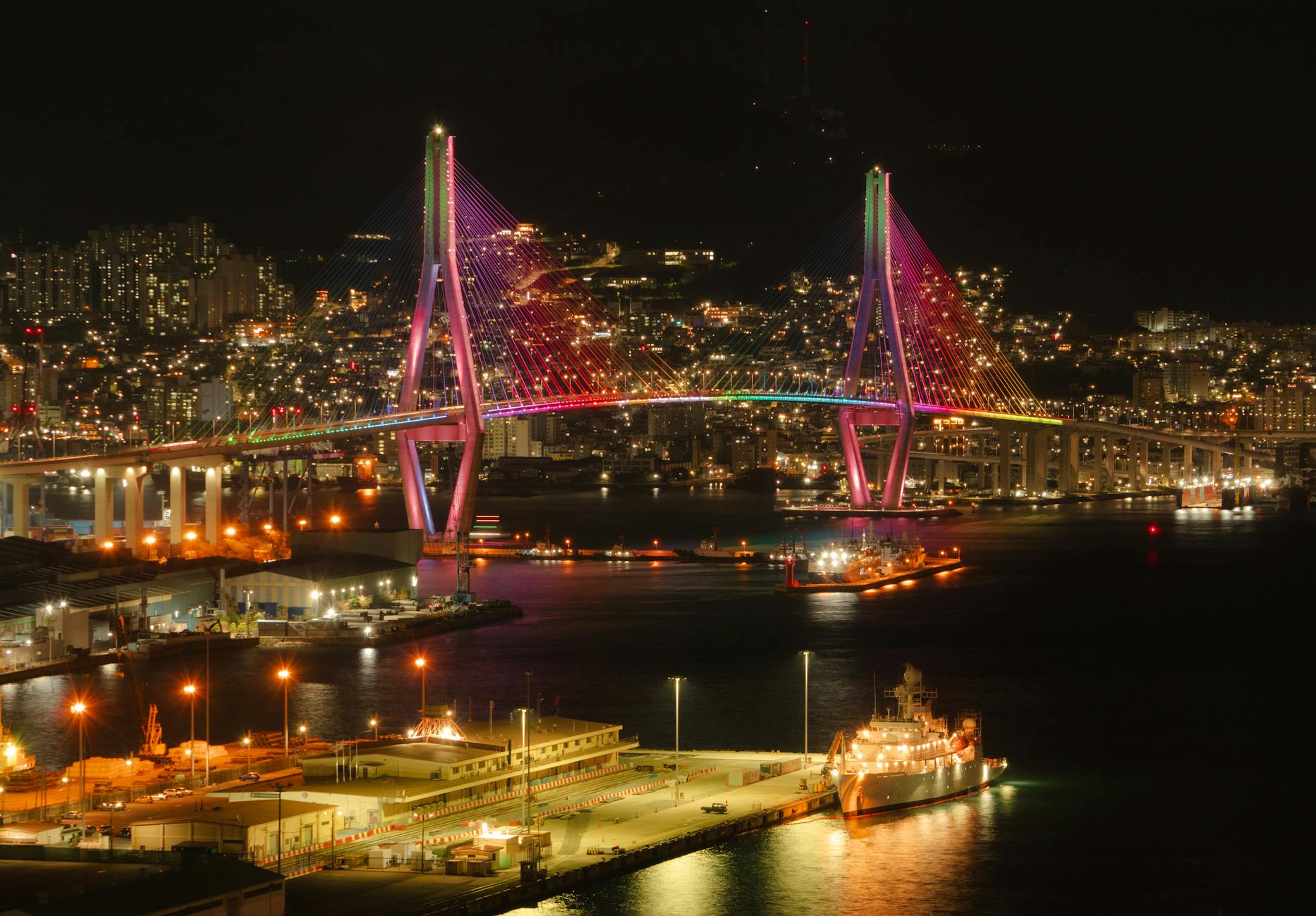 Stunning night view of the illuminated Busan Harbor Bridge, showcasing vibrant cityscape lights.