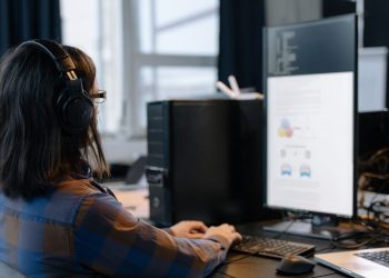 IT professional working on a computer in a modern office setting, focused on coding and tasks.