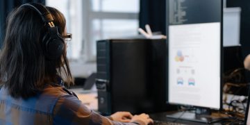 IT professional working on a computer in a modern office setting, focused on coding and tasks.
