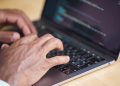 Hands typing on a laptop with code displayed on screen, showcasing technology use.