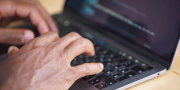 Hands typing on a laptop with code displayed on screen, showcasing technology use.