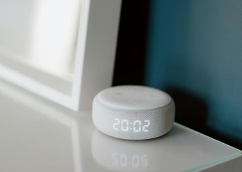 Close-up of a smart speaker with an illuminated 20:02 LED clock display on a desk.