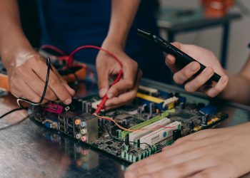 Close-up of hands working on a motherboard using electrical tools and tester.