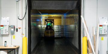 A forklift unloading goods at an industrial loading dock inside a warehouse.