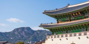 View of Gyeongbokgung Palace with traditional Korean architecture set against a mountain backdrop on a sunny day.