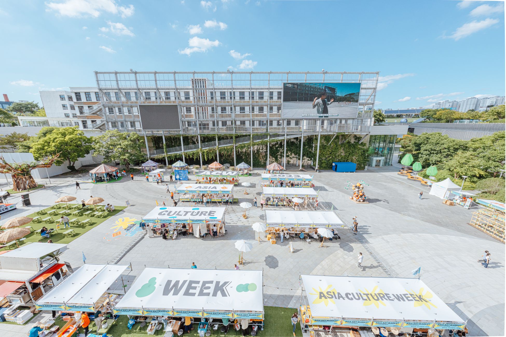 A vibrant outdoor market celebrating Asia Culture Week with stalls and greenery.