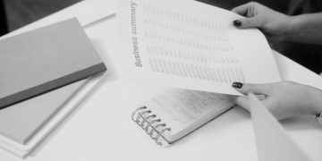 Black and white image of a businesswoman reviewing a business summary on paper.