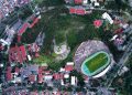 Aerial view of a city stadium encircled by lush greenery and urban architecture.