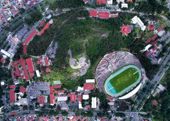 Aerial view of a city stadium encircled by lush greenery and urban architecture.
