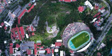 Aerial view of a city stadium encircled by lush greenery and urban architecture.