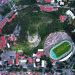 Aerial view of a city stadium encircled by lush greenery and urban architecture.