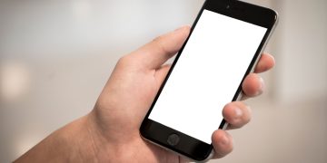 A hand holding a modern smartphone with a blank screen, ideal for design mockups.