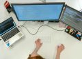 A female software engineer coding on dual monitors and a laptop in an office setting.