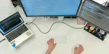 A female software engineer coding on dual monitors and a laptop in an office setting.