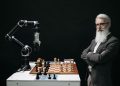 A robotic arm and a bearded man engaged in a strategic chess game highlighting technology and innovation.