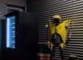 A dimly lit industrial room features a vending machine beside a quirky robot sculpture.