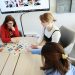 Three women playing a card game at an office table, fostering teamwork.