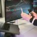 A professional analyzing financial charts on computer monitors and a smartphone, symbolizing digital finance strategies.