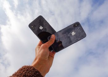 Close-up of a hand holding two smartphones against a cloudy sky, showcasing modern technology.