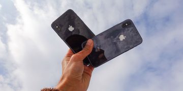 Close-up of a hand holding two smartphones against a cloudy sky, showcasing modern technology.