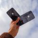 Close-up of a hand holding two smartphones against a cloudy sky, showcasing modern technology.