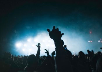 Exciting concert scene with people raising hands, set against stunning lights.