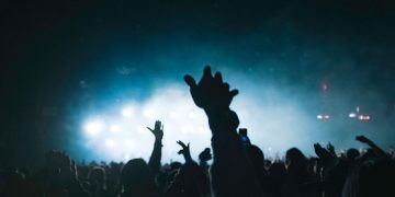 Exciting concert scene with people raising hands, set against stunning lights.