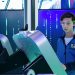 Teenager interacts with futuristic device using VR goggles in tech environment.