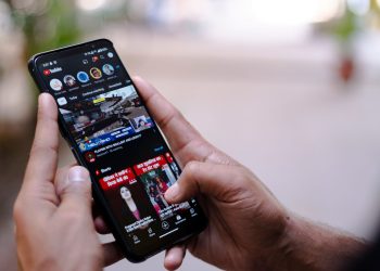 Close-up of hands using a smartphone to watch YouTube outdoors, showcasing digital connectivity.