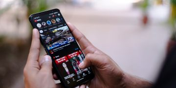 Close-up of hands using a smartphone to watch YouTube outdoors, showcasing digital connectivity.