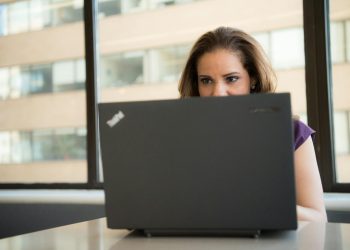 Focused woman using a laptop in a brightly lit office setting, showcasing modern work technology.