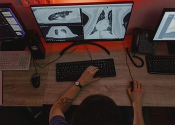 A radiologist reviews x-ray scans on multiple monitors at a desk, focusing on medical diagnostics.