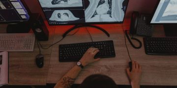 A radiologist reviews x-ray scans on multiple monitors at a desk, focusing on medical diagnostics.