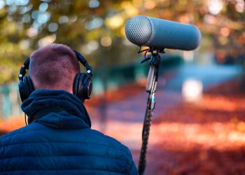 Audio professional recording outdoors in a vibrant autumn park with headphones and microphone.