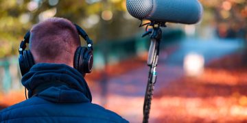 Audio professional recording outdoors in a vibrant autumn park with headphones and microphone.