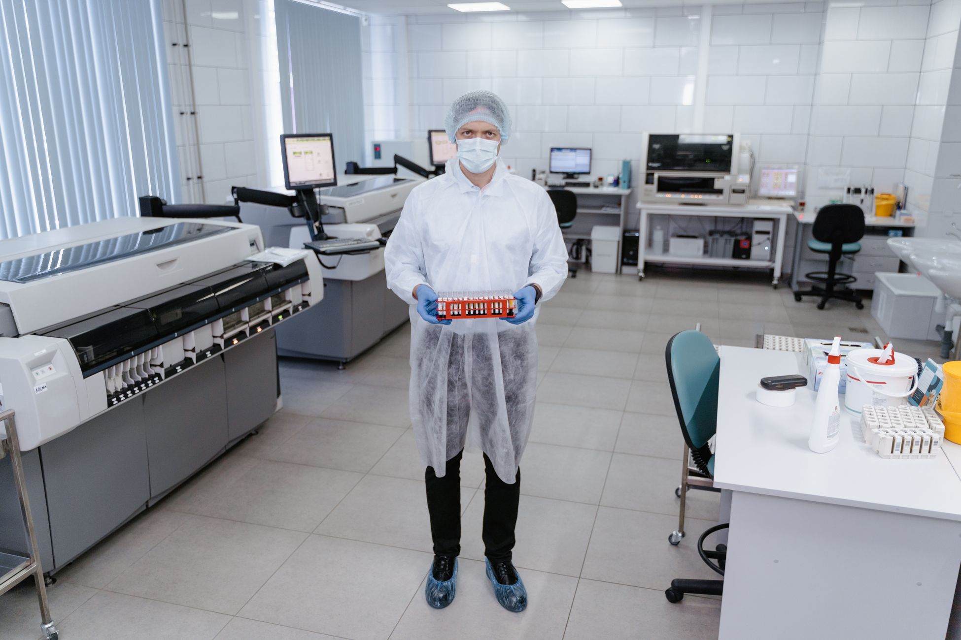 Scientist in PPE holding test samples in a modern laboratory setting.